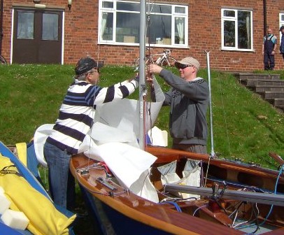 A sailing instructor shows a trainee how to rig up a dinghy