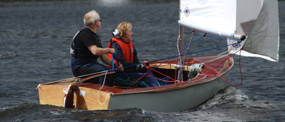 An instructor demonstrates sailing a dinghy downwind to a novice crew